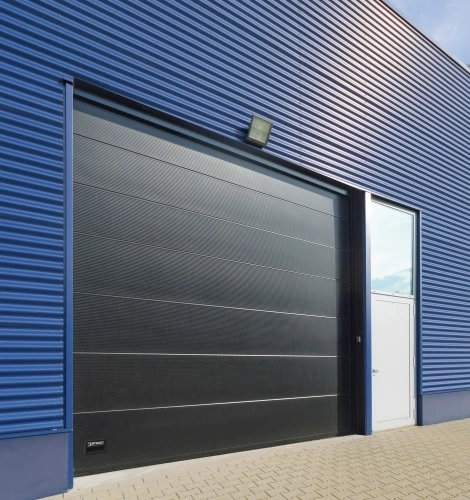 Industriële sectiedeur bij blauwe bedrijfsgevel – zwarte garagedeur met loopdeur